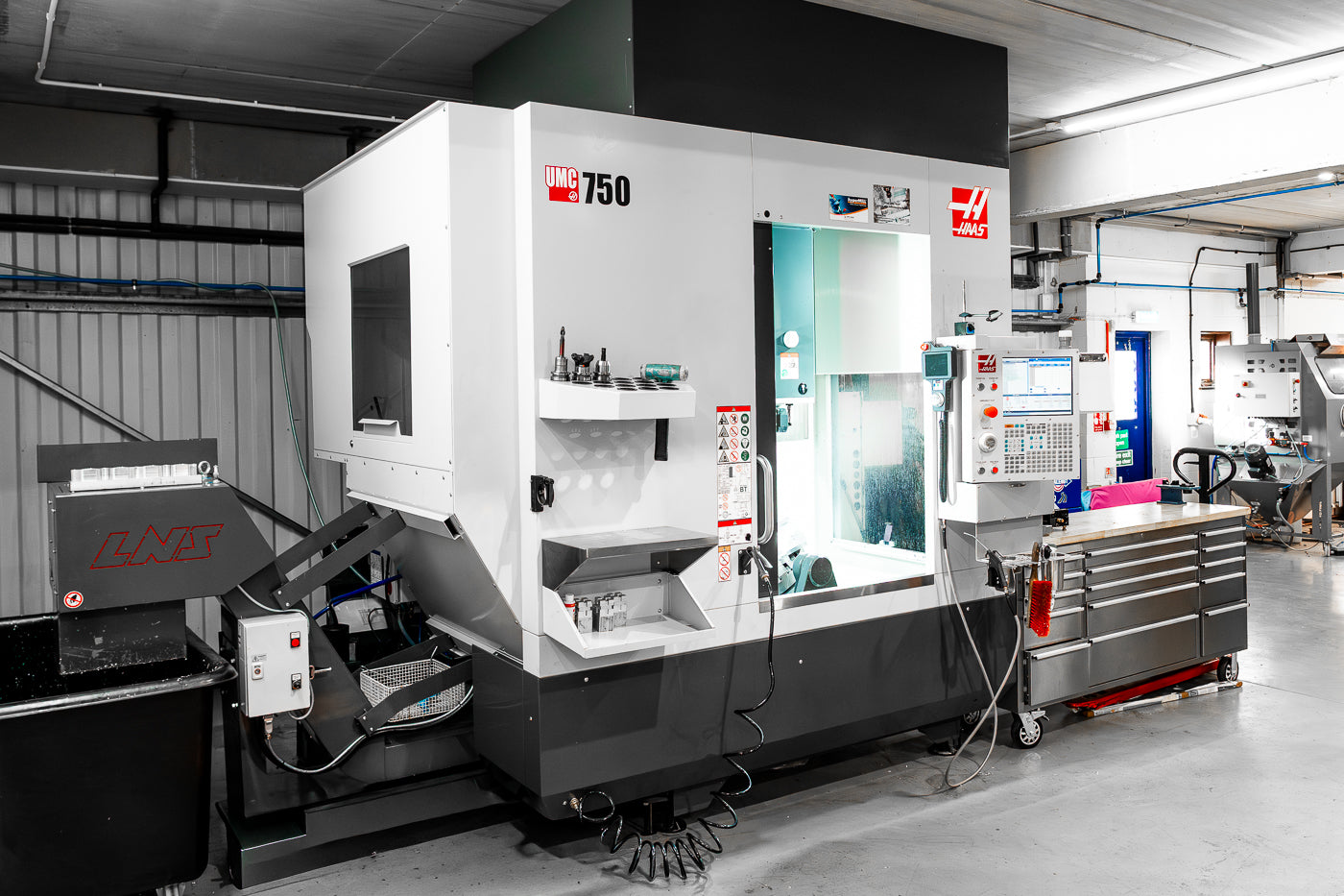 CNC 5 axis machine in a workshop setting with various tools and equipment around